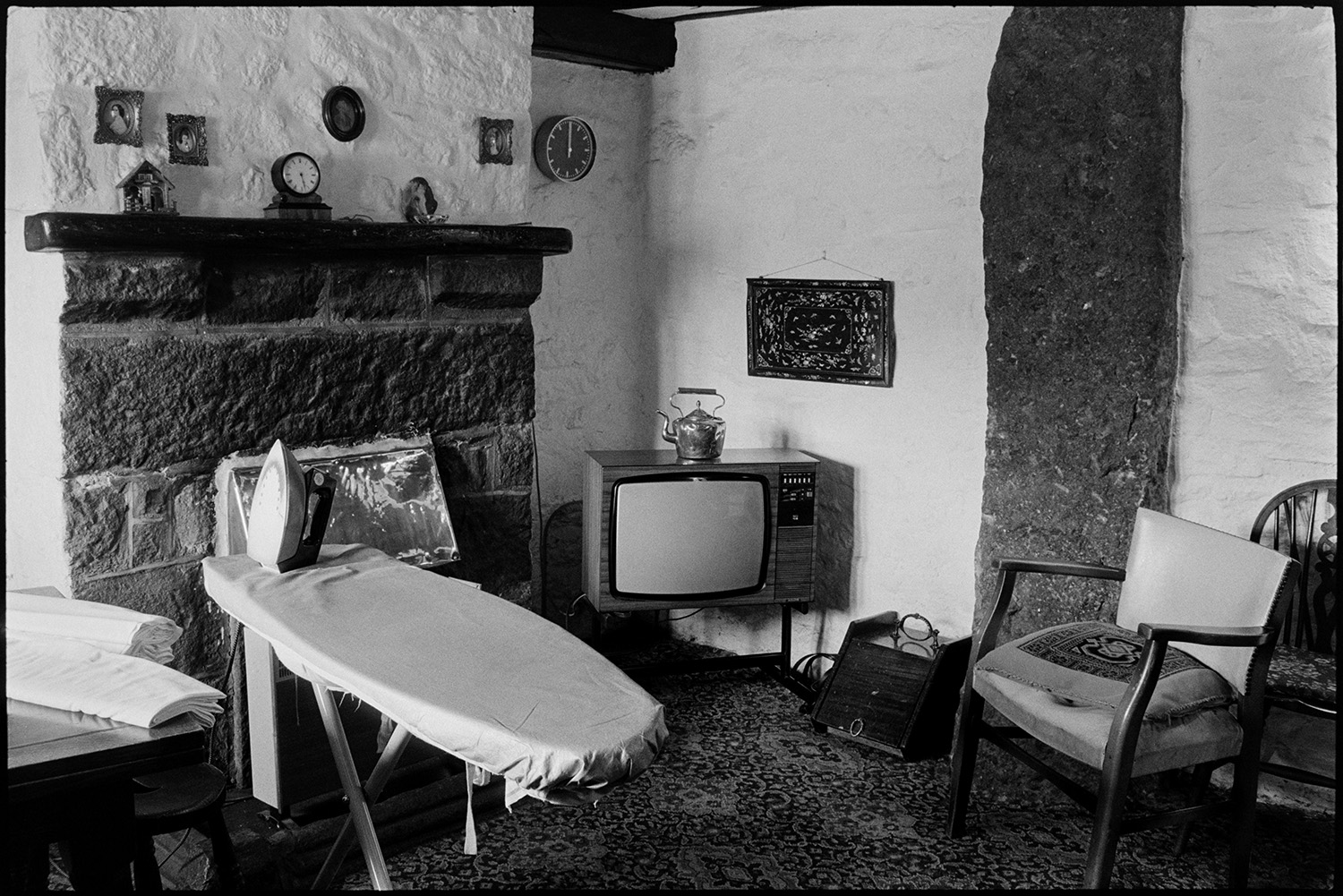 Woman ironing in pub sitting room with television, fireplace. Pub bar.
[A corner of the bar area at the Kings Arms, South Zeal with fireplace, ironing board, chair and television.]