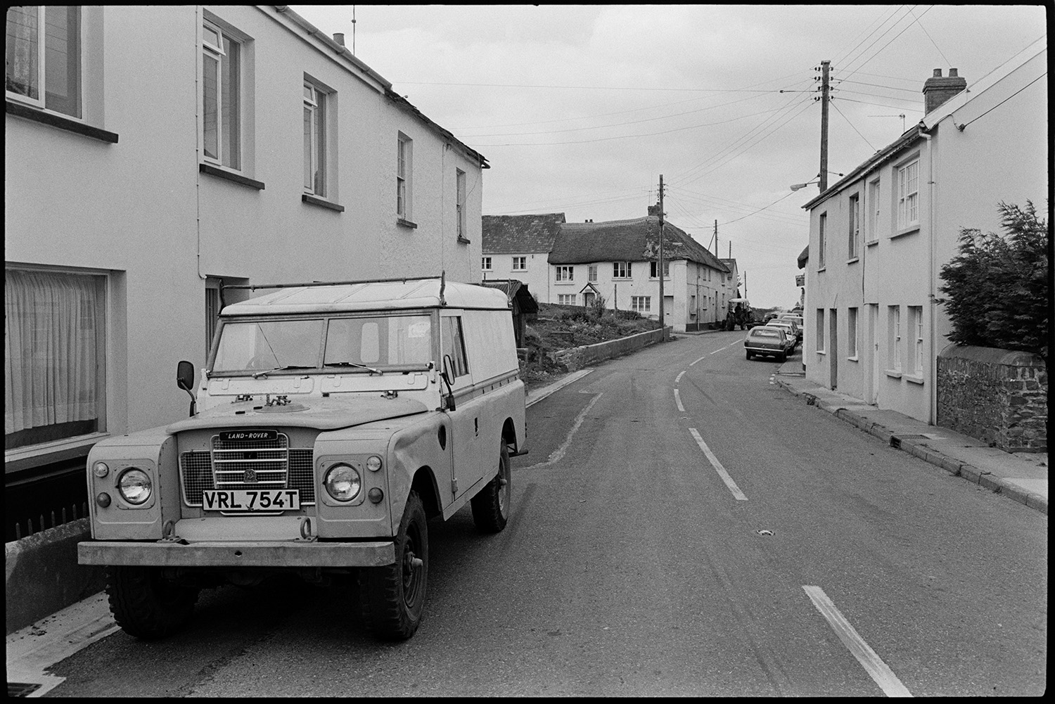 Street scenes with Land Rover. Comparison with old photos.
[A Land Rover parked in a street at Beaford with cottages, parked cars and a tractor driving up the road.]