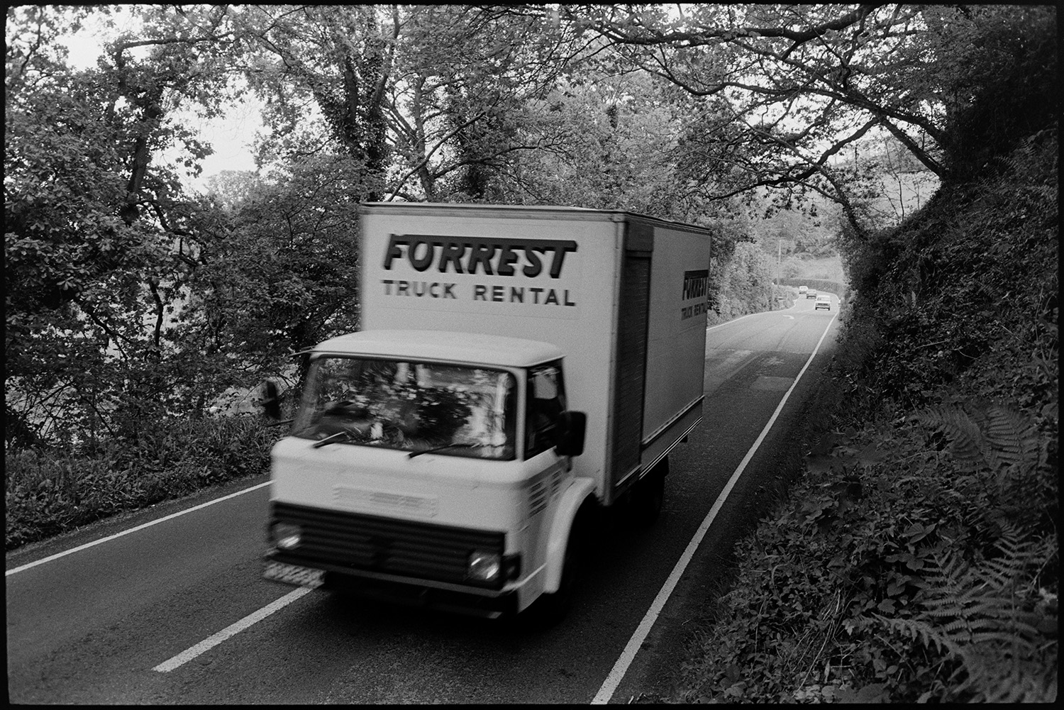 Lorries and cars on road.
[A Forrest truck rental lorry driving up Kingford Hill, High Bickington.]