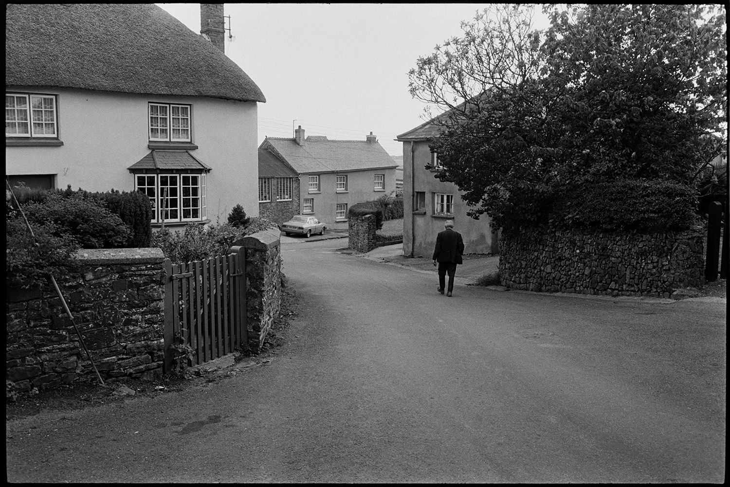 Scenes around village, comparison shots with old photos.
[A man walking down a street past a thatched cottage on the left in High Bickington.]