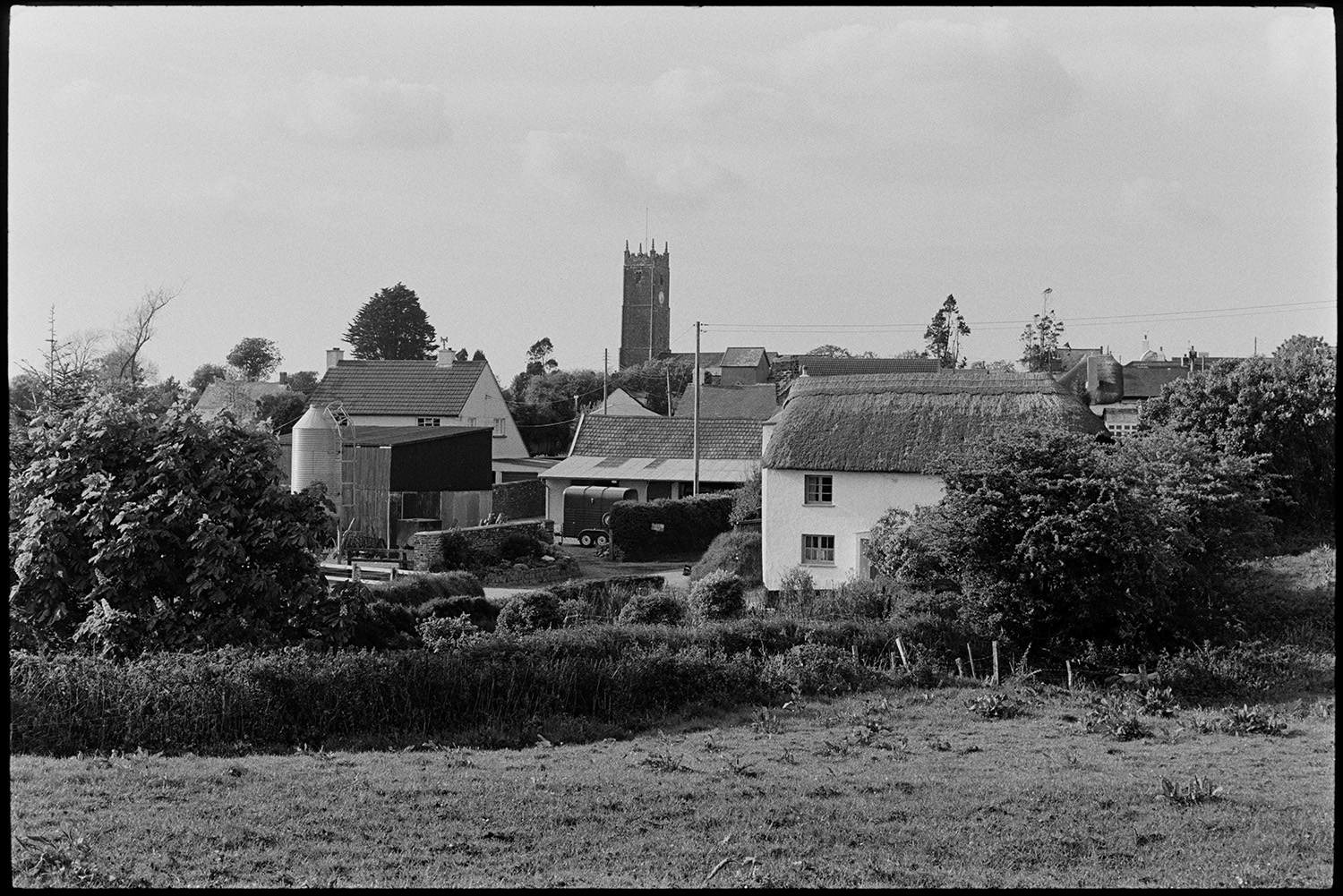 Scenes around village, comparison shots with old photos.
[A scene taken from a field of a thatched cottage and farmyard with a silo and horse box at High Bickington. The church tower is visible in the background.]