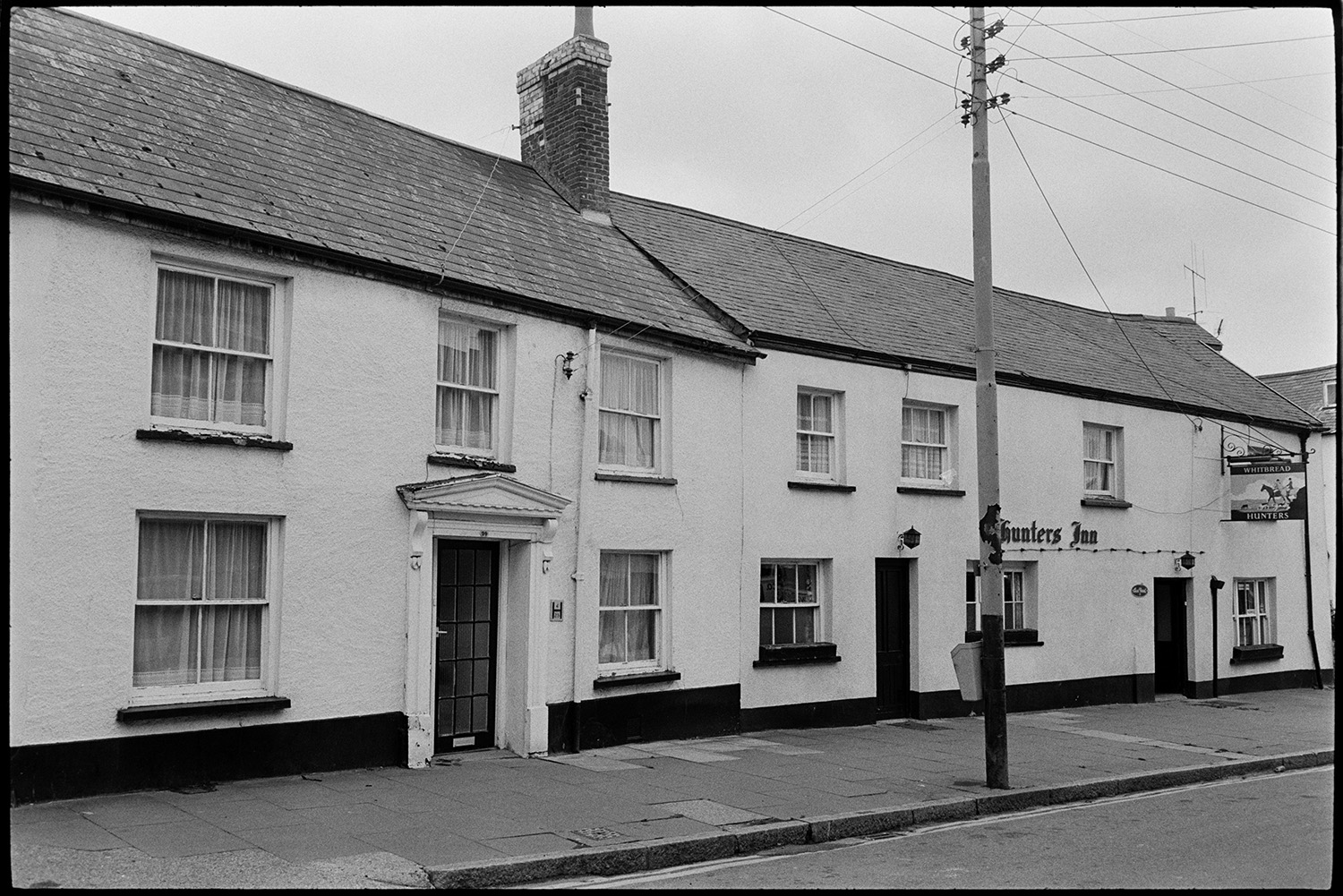 Scenes around town, comparison with old photos, railway line and station, lorries and cars, river.
[The front of The Hunters Inn at Torrington. The house next door is also visible on the street.]
