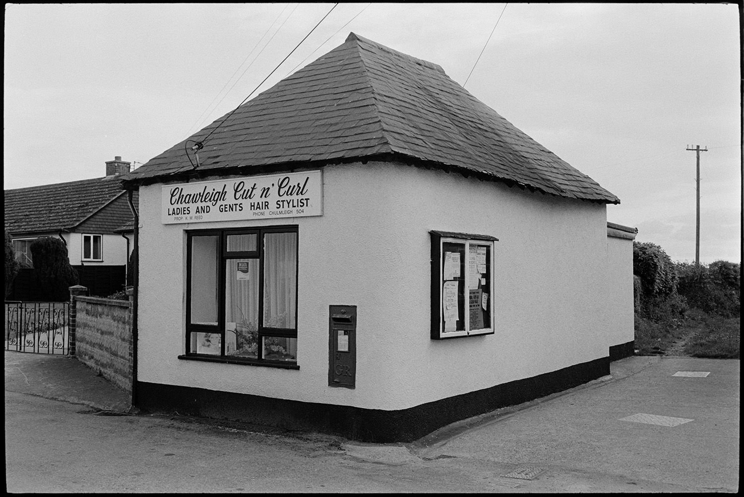 Hairdressing salon in village.
[The  shop front of 'Chawleigh Cut n' Curl' ladies and gents hair stylist in Chawleigh. A post box is set into the wall of the hairdresser and a noticeboard is on the other side of the building.]