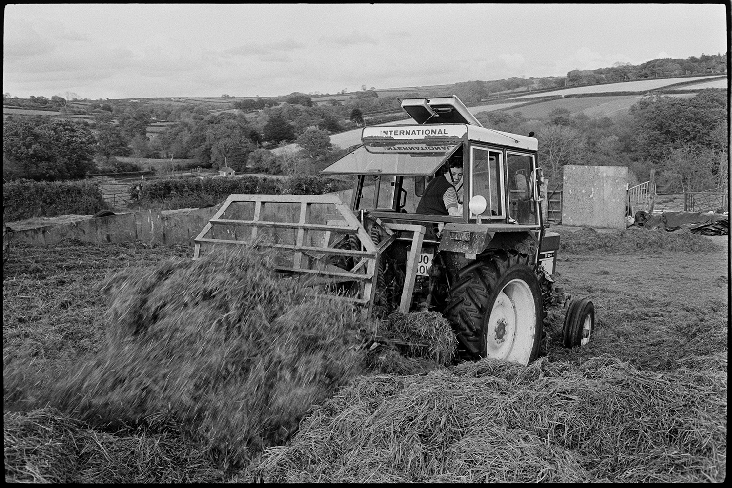 Tractors moving silage.
[A tractor being used to move silage in a field at Cleave Farm, Dolton, with surrounding fields and trees in the background.]