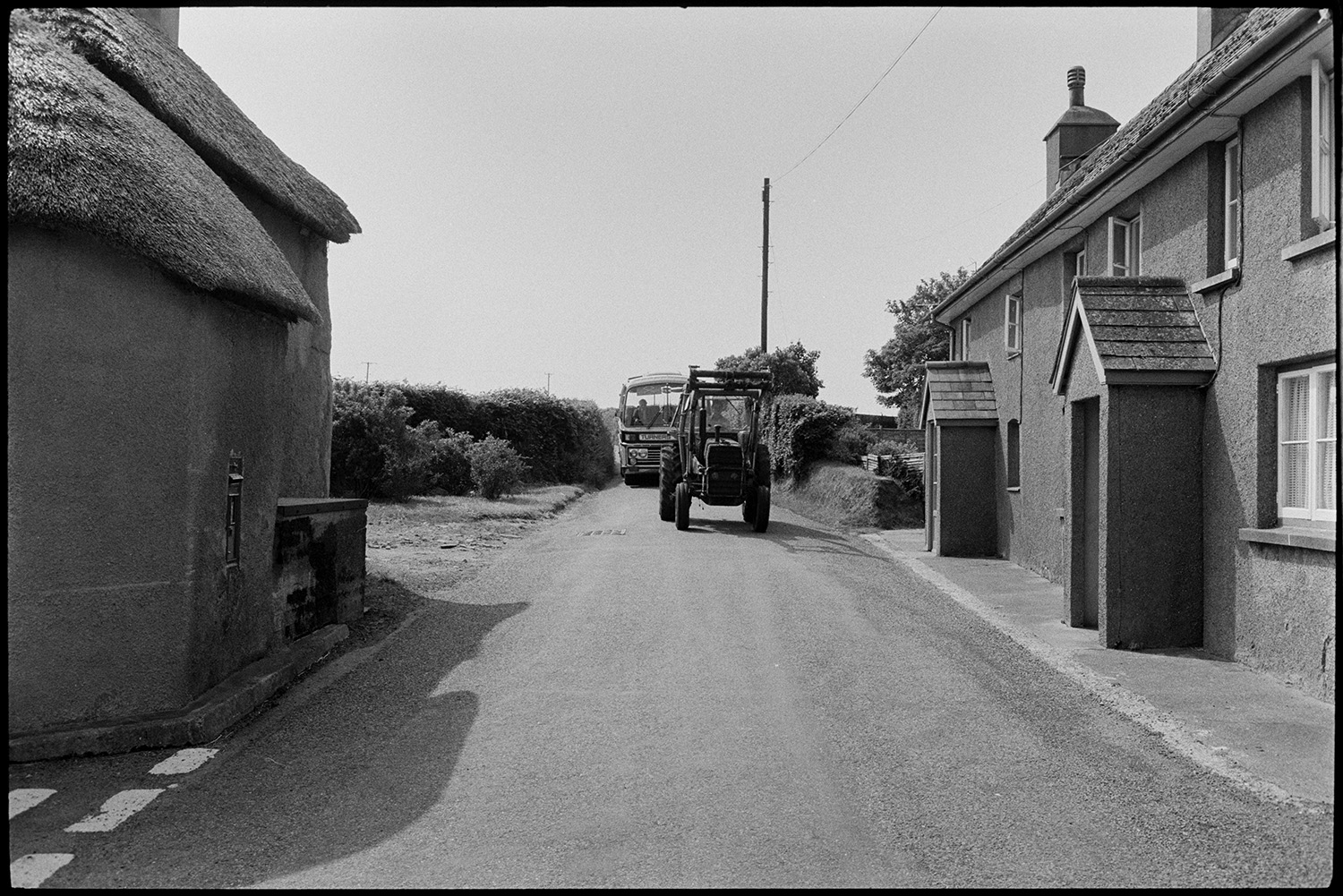 Road and houses, comparison with old photo.
[Tractor and a Turners coach driving past Moor End, Burrington, passing a thatched house with a post box set into the wall of the house.]