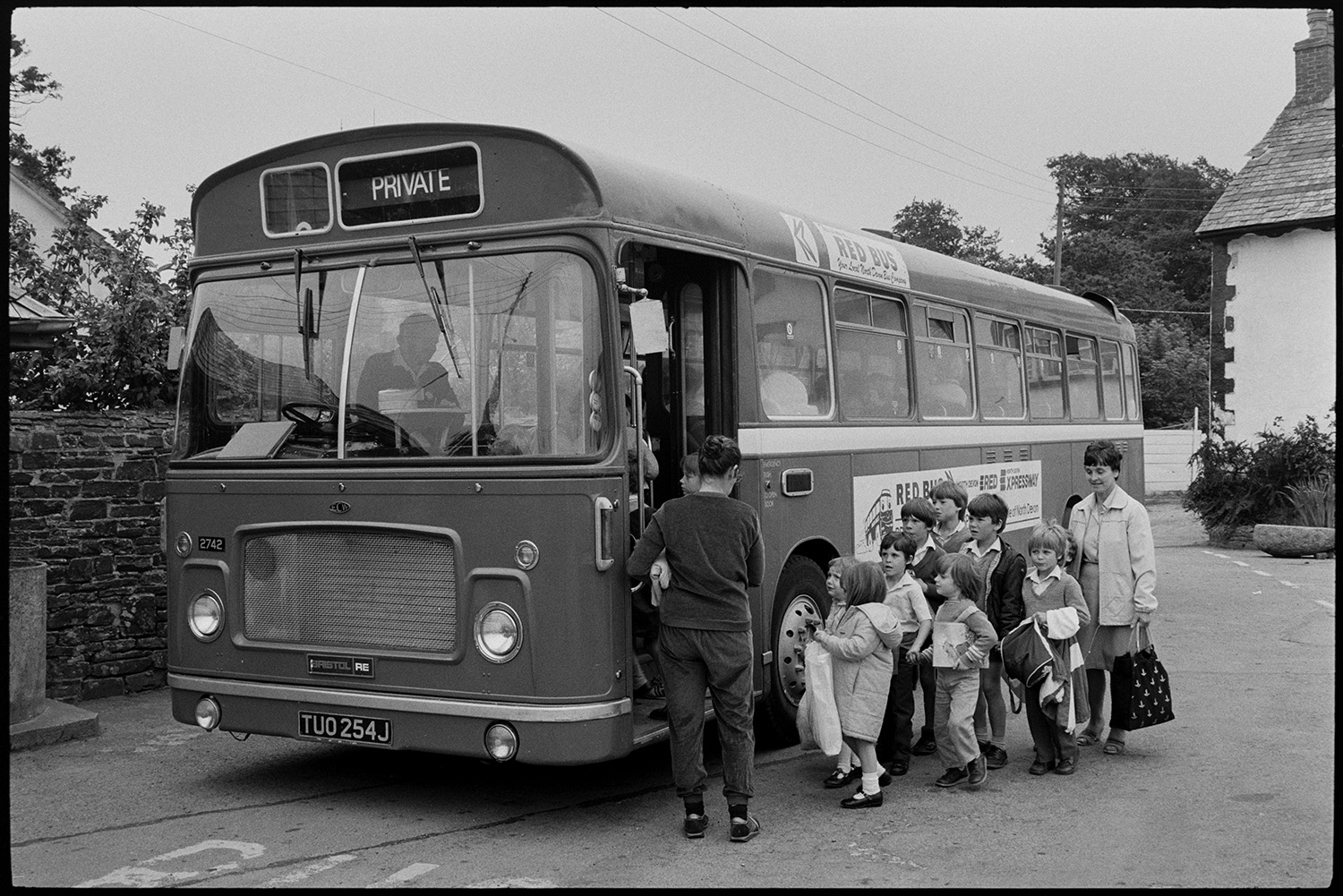 Schoolchildren getting onto bus for trip.
[A group of children from Dolton Primary School and two women, possibly teachers, getting a Red Bus Company bus parked in the bus stop in Dolton, to go on a school trip.]