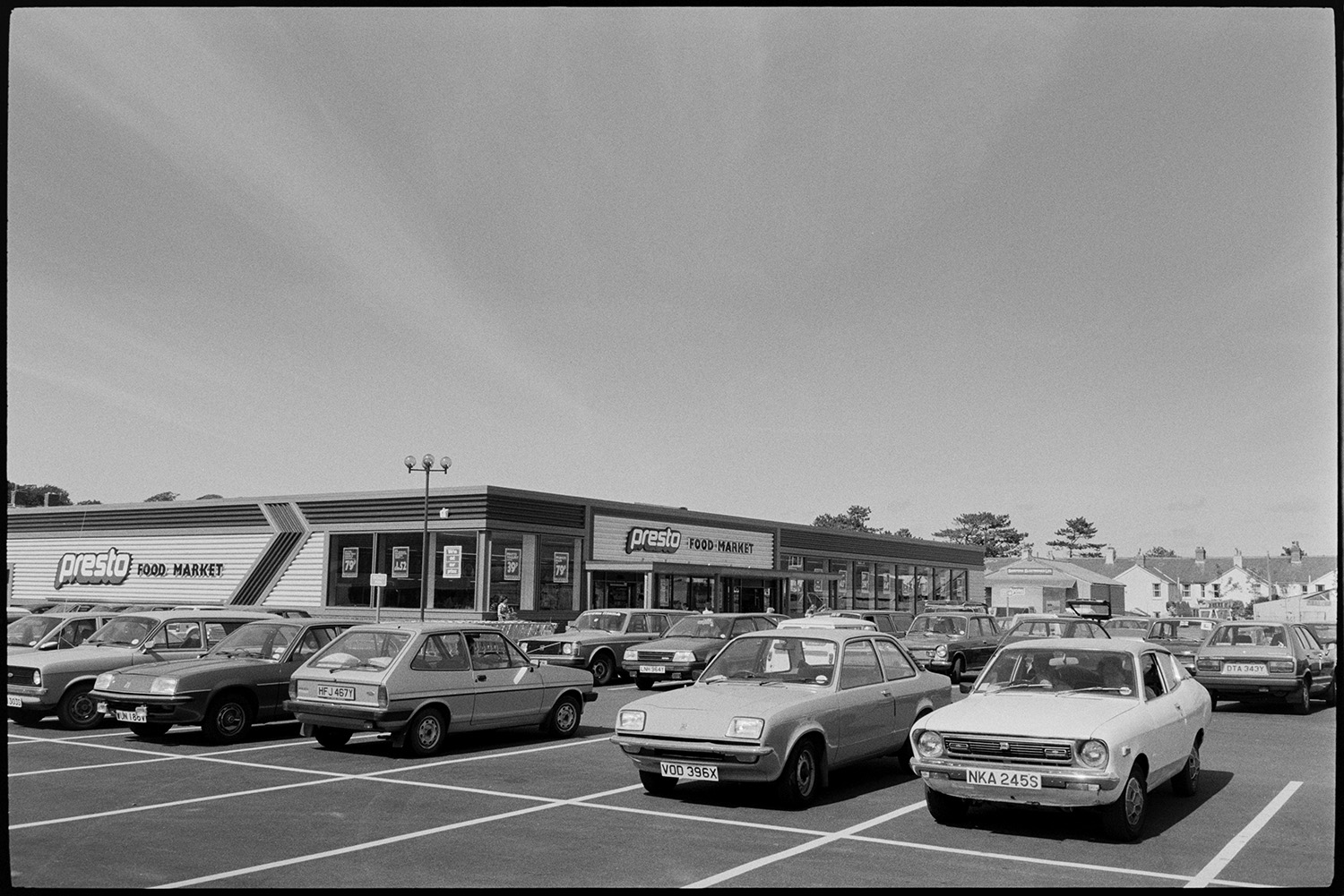 Interior of supermarket, people shopping, car park. Fruit, cash desk, check out.
[The car park and entrance to Presto Food Market in Bideford.]