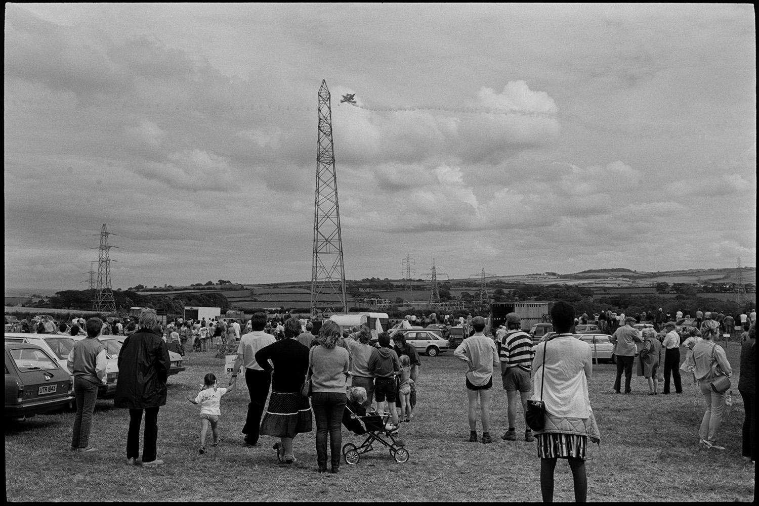 North Devon Show, Prize cattle, sheep, exhibitions etc.
[Spectators at the North Devon Show, near Alverdiscott, watching an aerial display. Parked vehicles and fields are visible in the background with electricity pylons.]