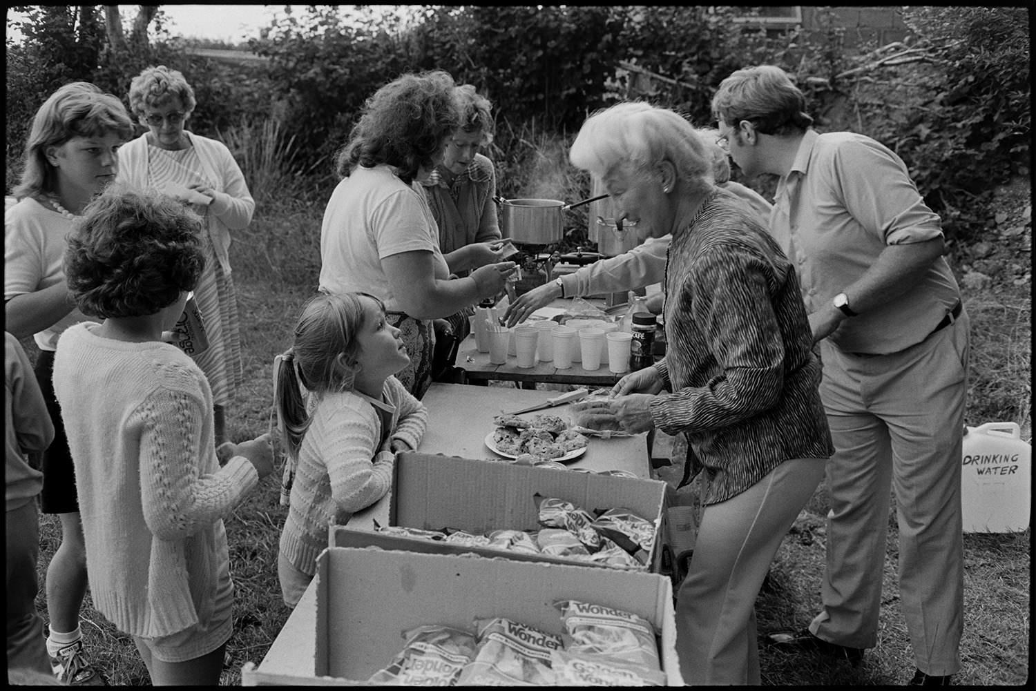 Flower show exhibits, jams, cups, sports, hot dog stall, bicycles, Clay Pigeon Shoot.
[Women and a man serving refreshments, including hot drinks and cakes, to women and children at the refreshment table at Dolton Flower Show.]