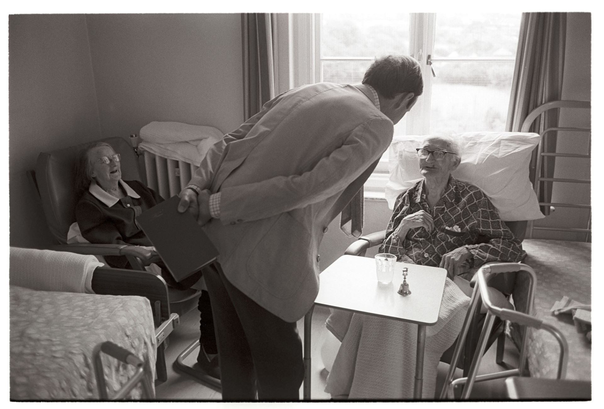 Doctor visiting patients in cottage hospital, elderly. 
[Doctor Richard Westcott visiting a man and woman in South Molton Cottage Hospital.]