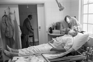 Dr Richard Westcott stitching a man's head by James Ravilious