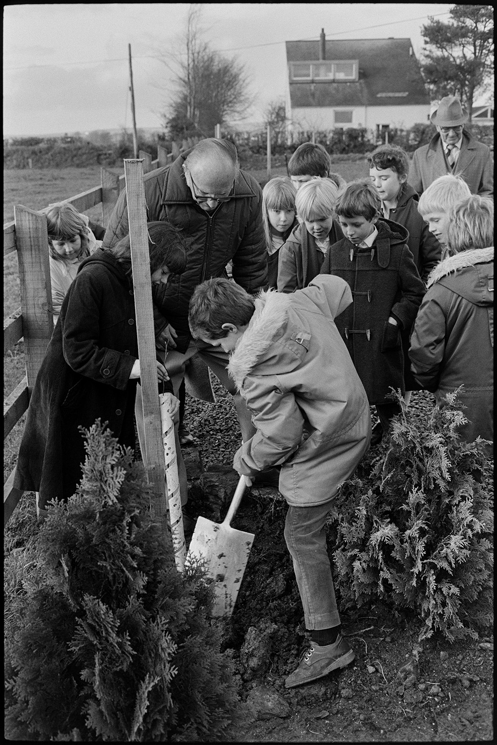 Tree planting ceremony. 
[Tree planting ceremony at the Beaford Centre. A boy is using a spade to dig a hole for the tree. Other children, a woman and a man are looking on.]