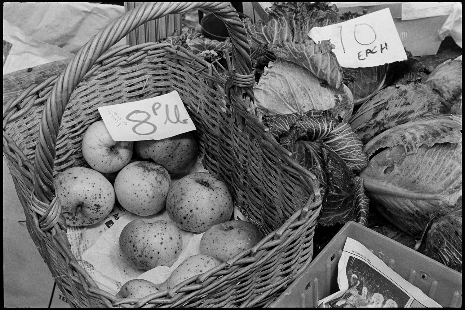 Pannier market, vegetables in baskets, potatoes, swedes, leeks.
[A basket of apples and an assortment of cabbages with price labels on a vegetable and fruit stall at Barnstaple Pannier Market.]