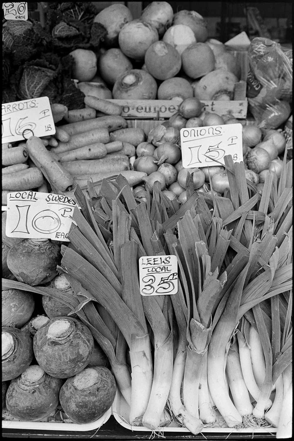 Pannier market, vegetables in baskets, potatoes, swedes, leeks.
[Swedes, leeks, onions, carrots, cabbages, potatoes and turnips with price labels on display on a vegetable stall at Barnstaple Pannier Market.]