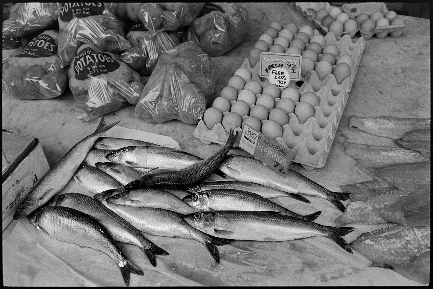 Fish and eggs on display.
[Bags of potatoes, trays of eggs, and herring fish, for sale at Barnstaple Pannier Market.]