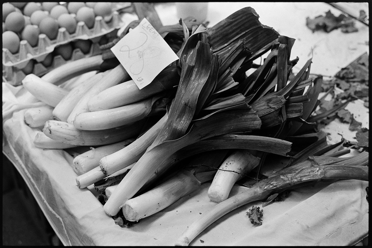 Pannier market, vegetables on display, cabbages, leeks, basket.
[A pile of leeks for sale, alongside trays of eggs, at Barnstaple Pannier Market. A price tag is displayed on the leeks.]