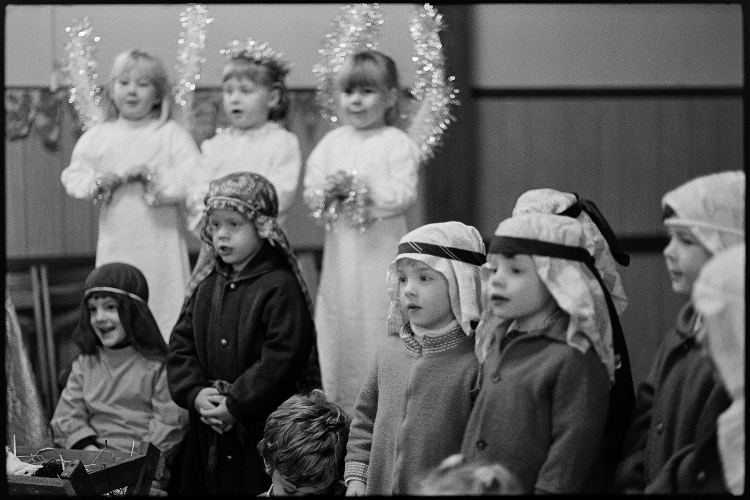 Christmas, children's Nativity play, singing carols.
[Children in costume performing a Christmas Nativity play in Dolton village hall. They are singing a carol.]