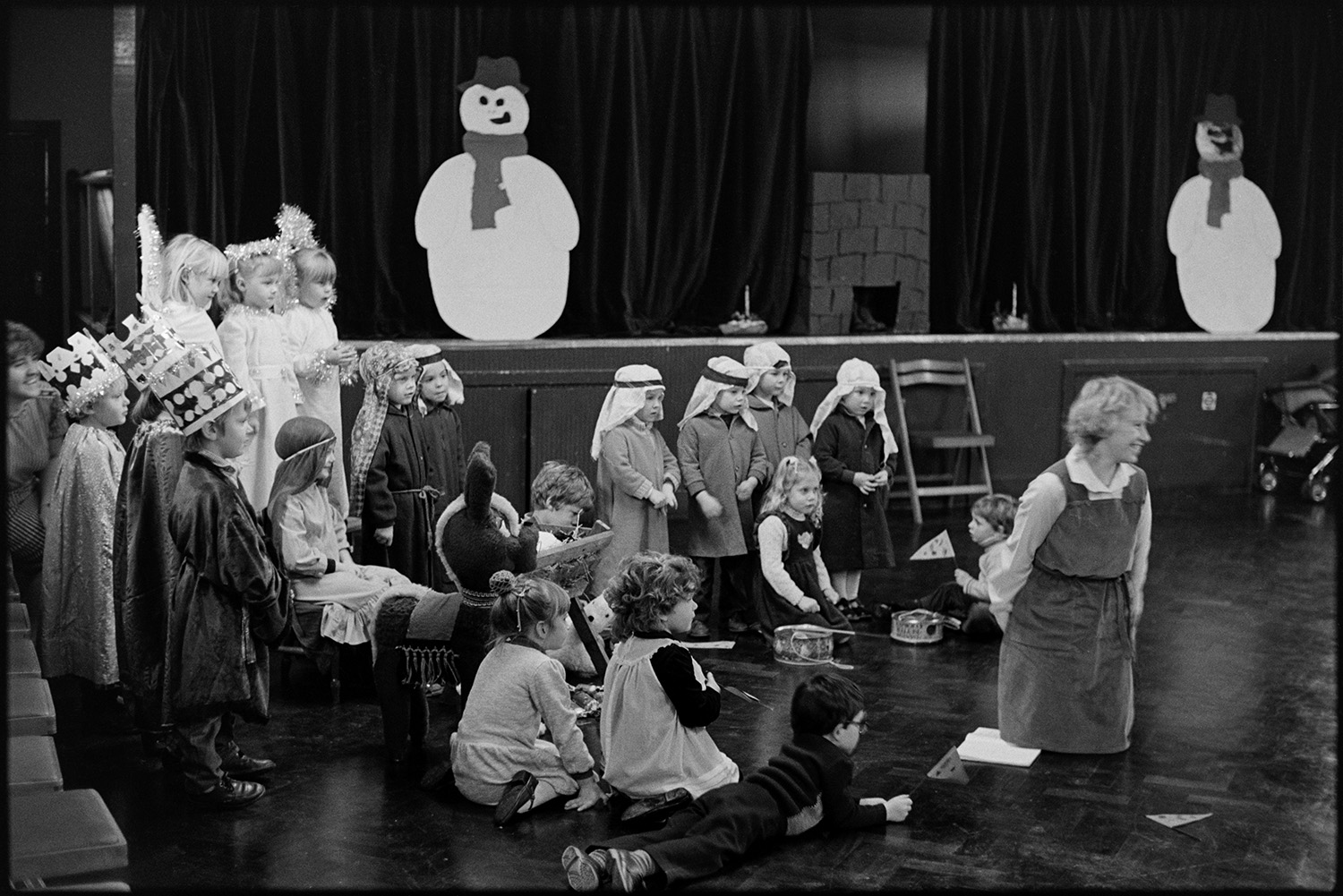Christmas, children's Nativity play, singing carols.
[Children in costume performing a Christmas Nativity play in Dolton village hall, with snowman models on the stage.]