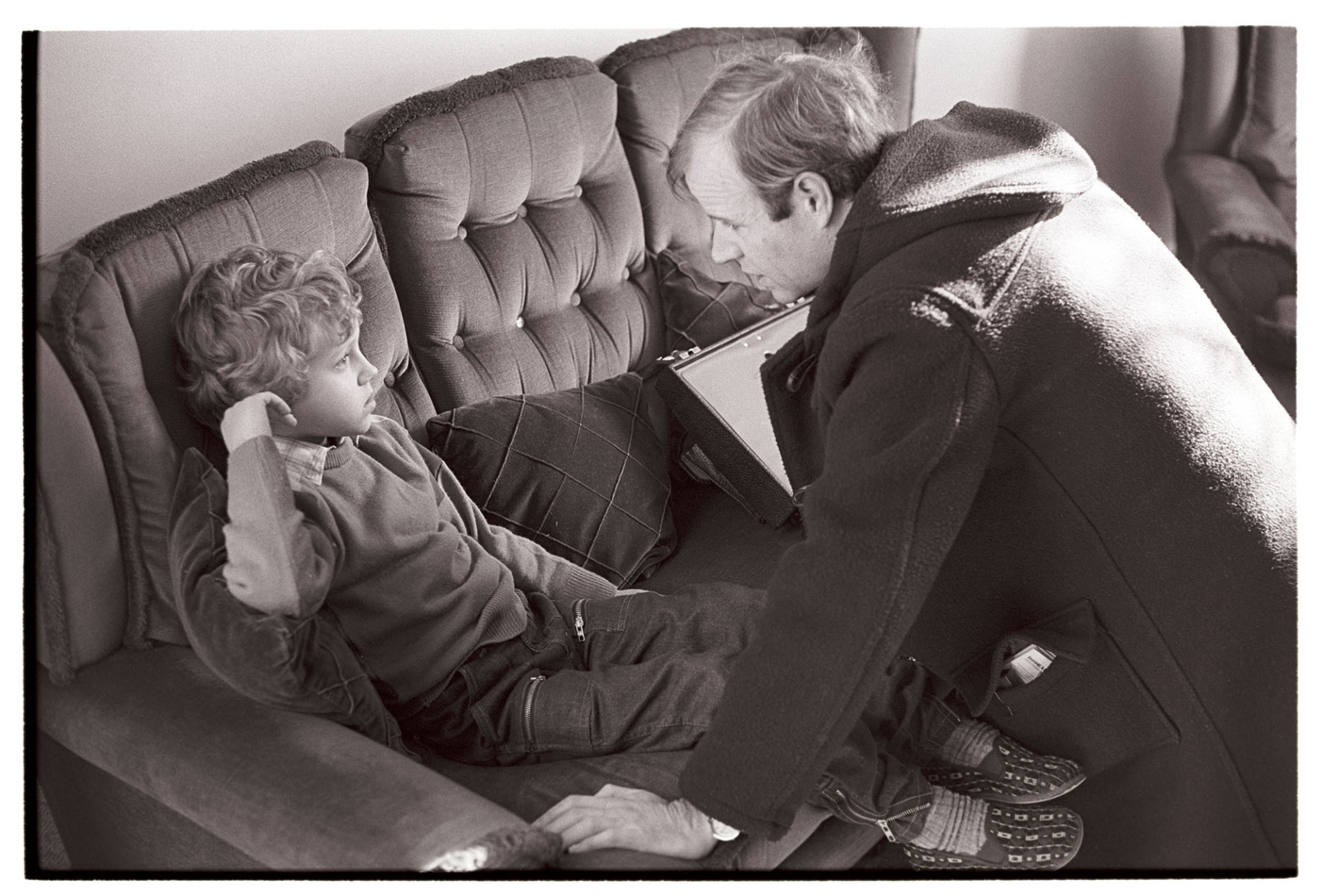 Doctor visiting sick child with mother in their home, boy on settee. 
[Doctor Richard Westcott visiting a sick boy at his home in South Molton. The child is sat on a sofa.]