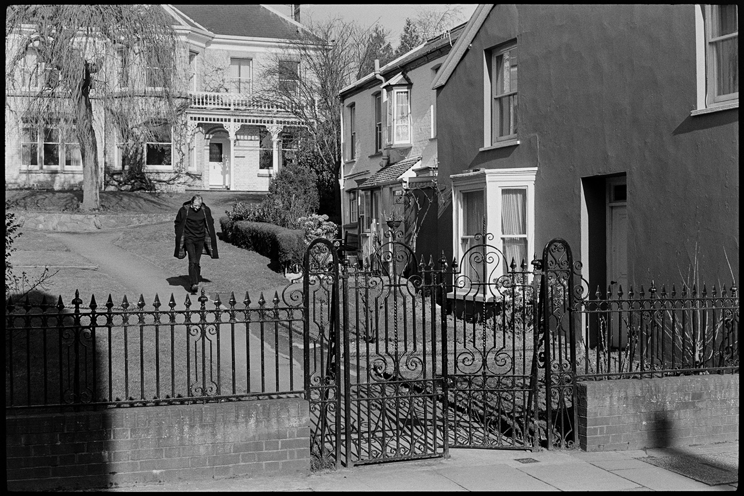 Doctor walking to see patients. 
[Doctor Richard Westcott walking past houses behind a gated entrance on his rounds to visit patients in South Molton.]