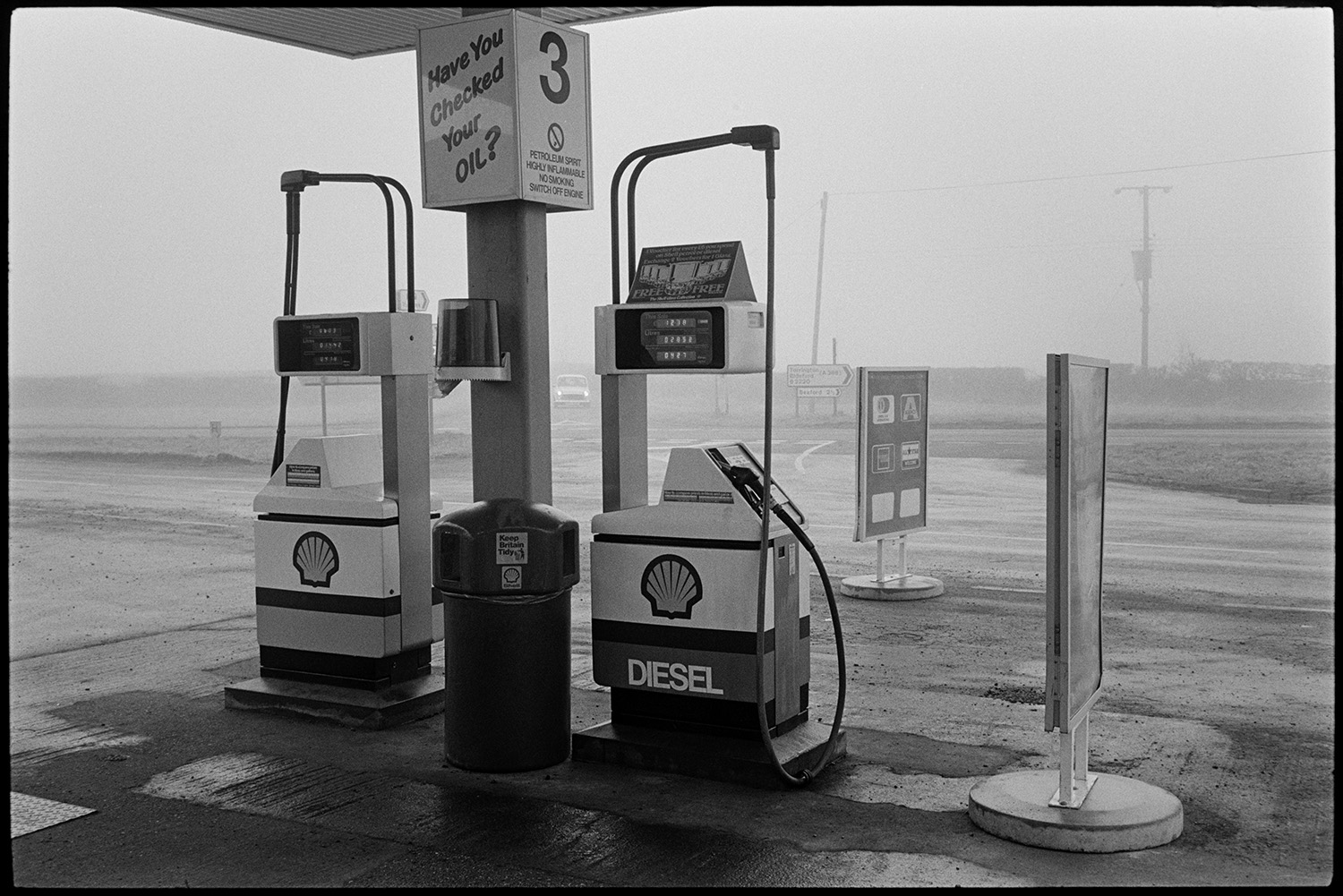 Men working in garage, tools, oil cans, tyres, mending puncture. 
[Petrol pumps on the forecourt at Dolton Beacon Garage.]