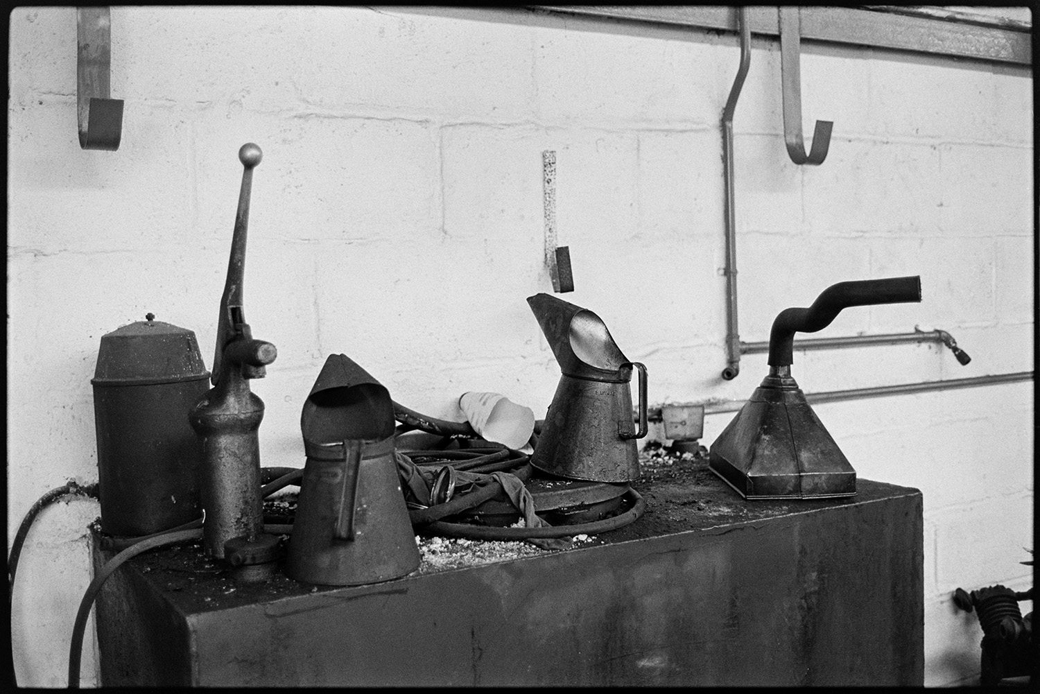 Men working in garage, tools, oil cans, tyres, mending puncture. 
[Various metal cans and machinery parts on a metal table at Dolton Beacon Garage.]