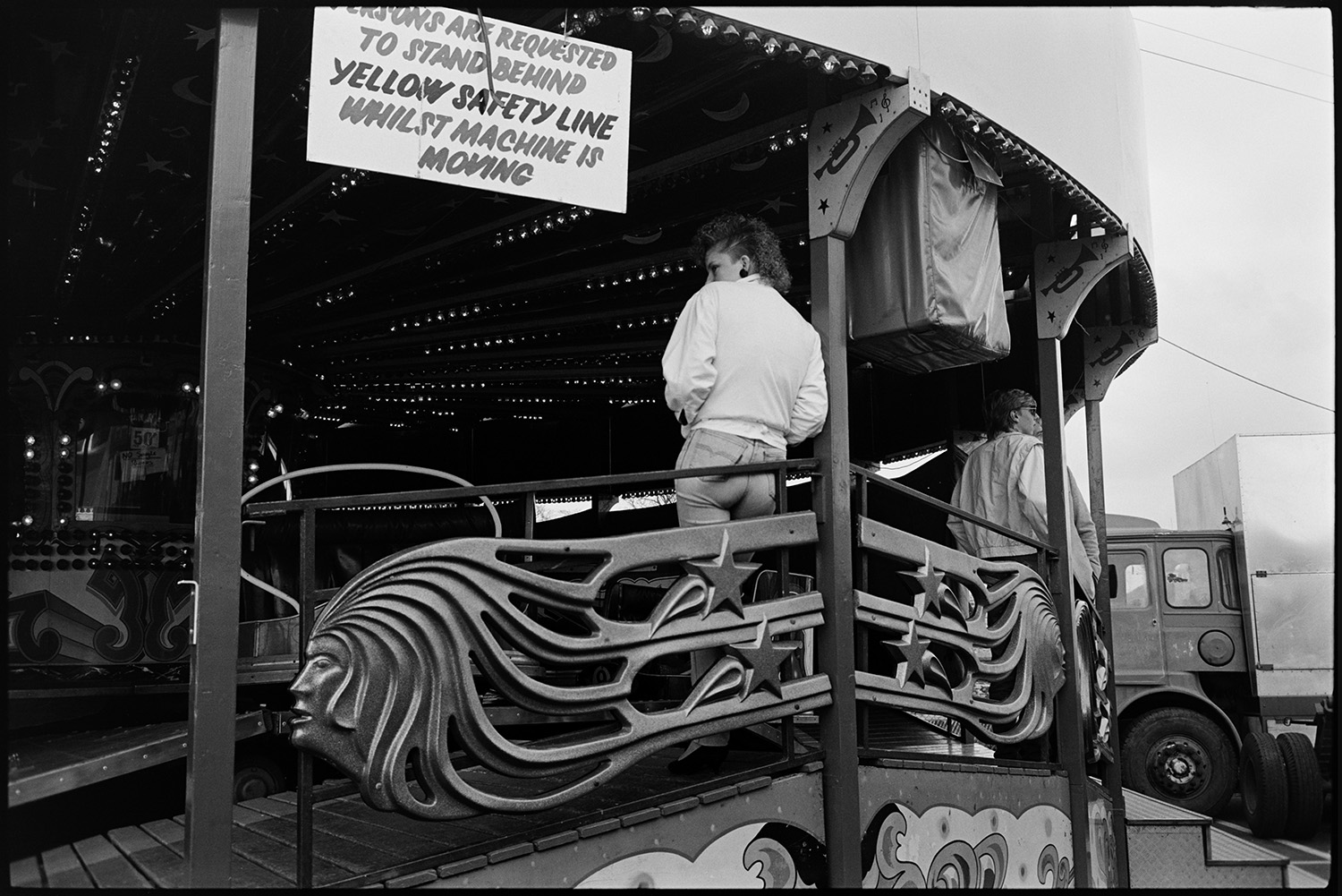 May Fair floats. Fairground procession. Generator lorry. Merry-go-round. 
[Teenagers watching the 'Waltzer' fairground ride at Torrington May Fair.]
