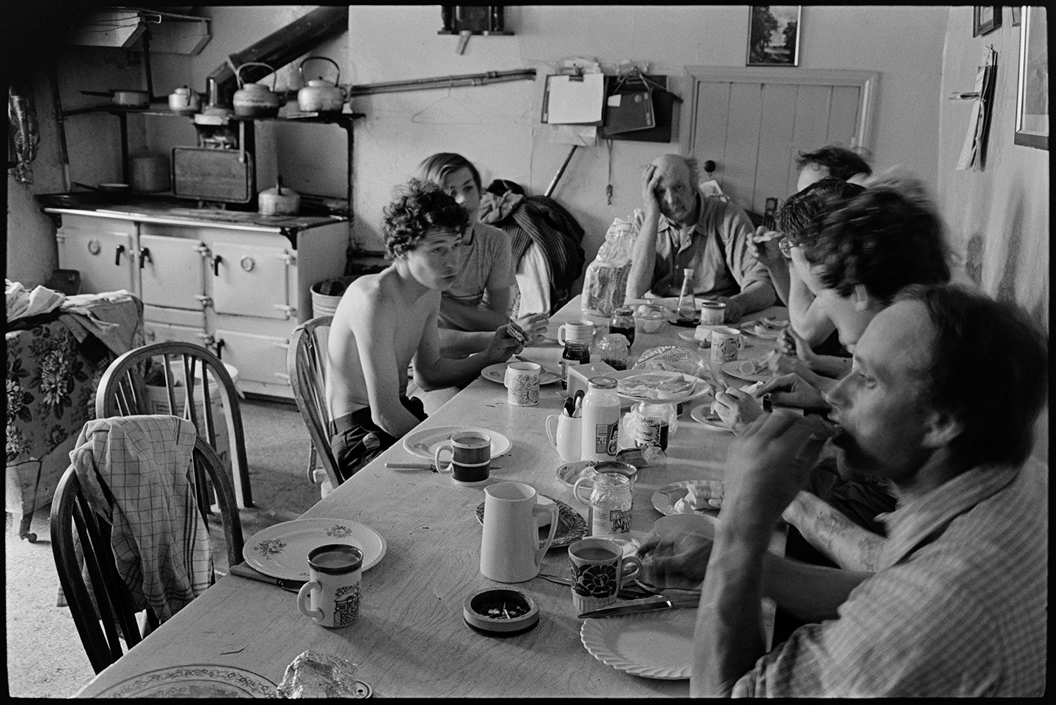 The French family sat having tea in their kitchen at Brendon Barton. A Rayburn stove can be seen in the background.