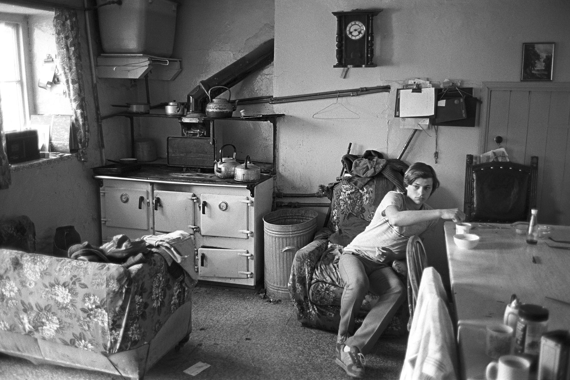 Man sitting in farmhouse kitchen having tea and watching cup final on television. 
[A young man from the French family sitting in his farmhouse kitchen at Brendon Barton, Exmoor, and watching the football Cup Final. His is stirring a mug of tea. In the background a sofa and rayburn stove is visible.]
