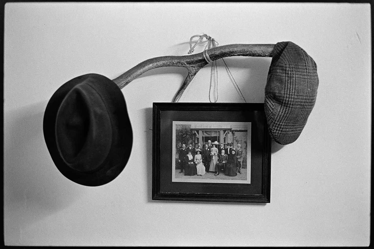 Hats and photograph hanging from antler hat stand. Cap mantelpiece. 
[An antler being used as a hat stand for a trilby hat and flat cap at Exmoor Farm. A photograph is also hung from the antler.]