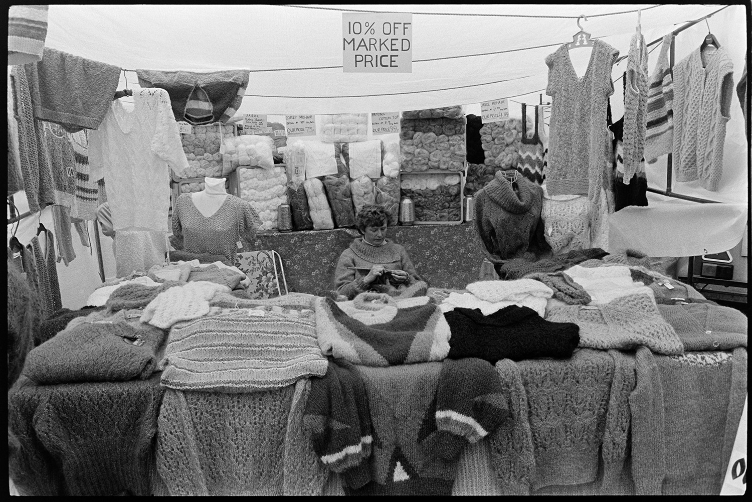 Knitting stall at fair? 
[A woman running a stall selling knitted jumpers and wool, possibly at a fair in Dolton.]