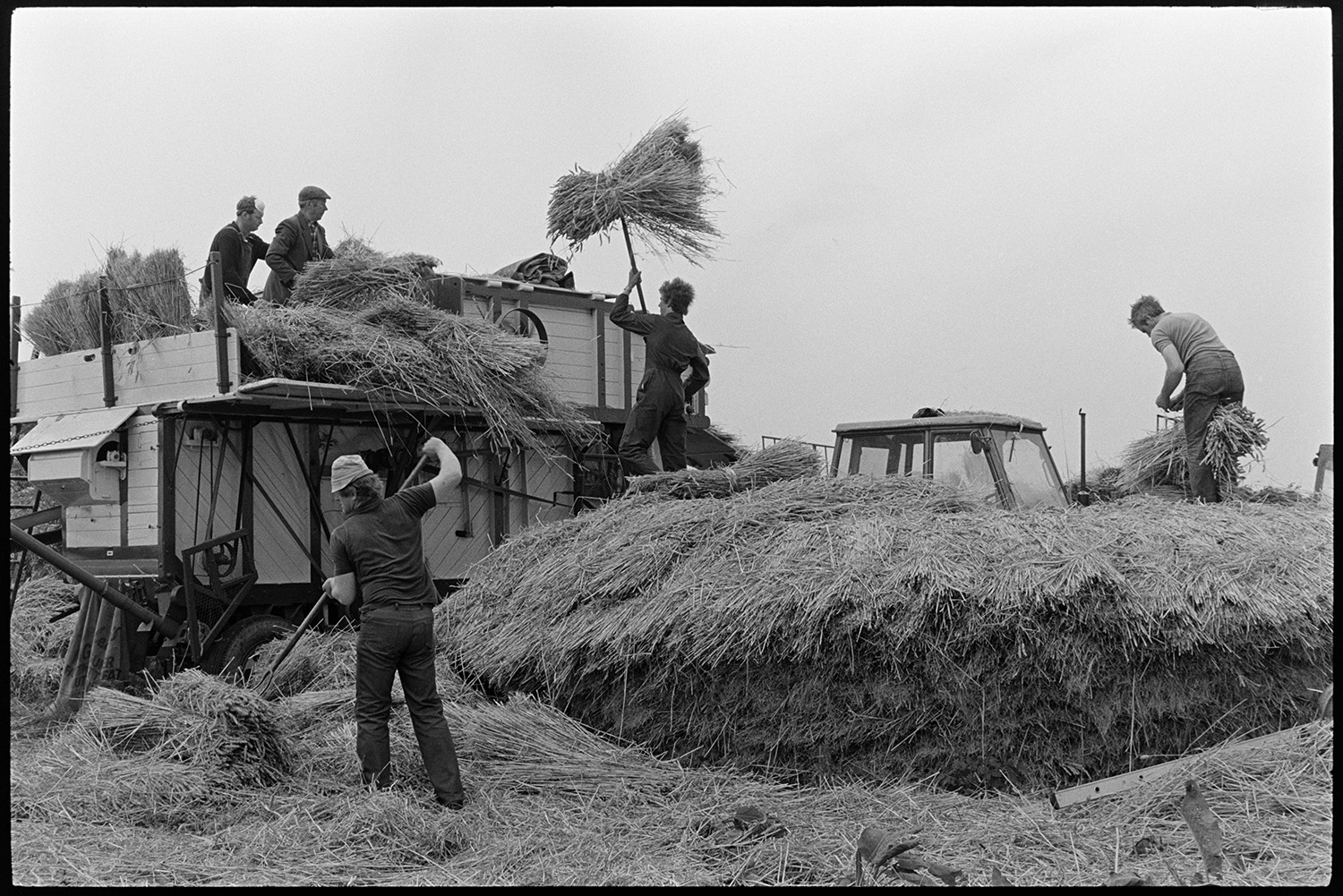 Reed comber at work, pile of ropes and spars. 
[Men dismantling a wheat rick and loading the reed into a reed comber, using pitchforks, in a field at Westacott Barton, Riddlecombe.]