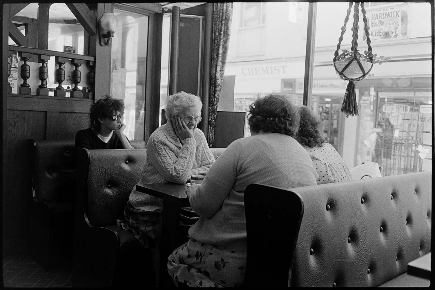 People sitting in restaurant having tea or coffee. 
[Women sat in a booth in a restaurant or café in Mill Street, Bideford. A young man is sat at the table behind them.]