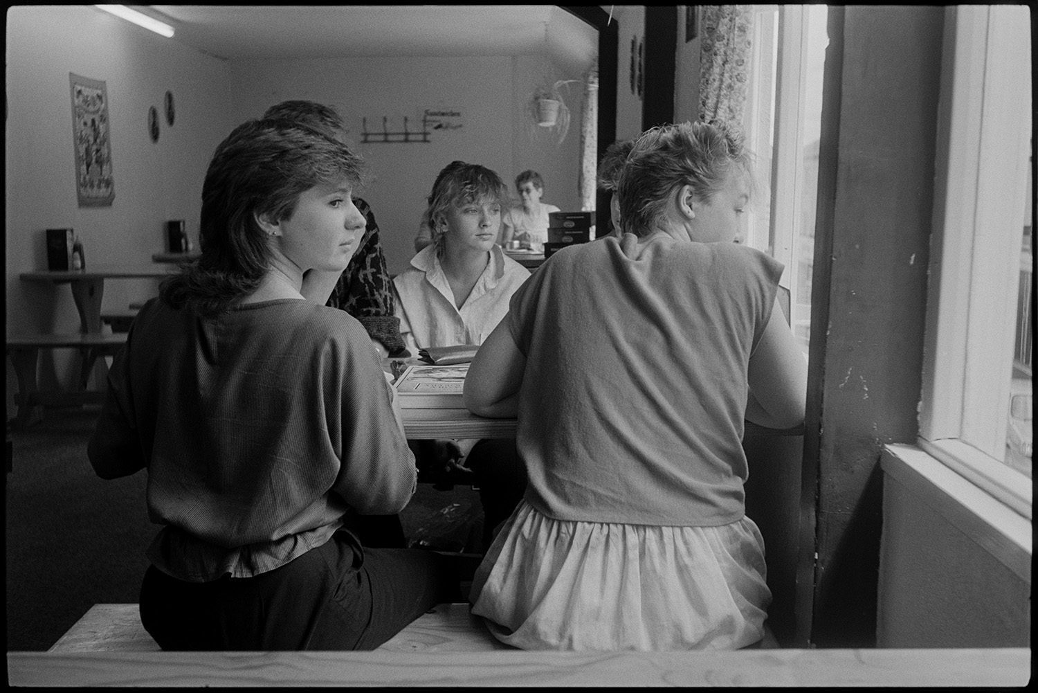 Girls sitting in café. 
[A group of girls sitting at a table in a café in South Street, Torrington. They are looking out of the window.]