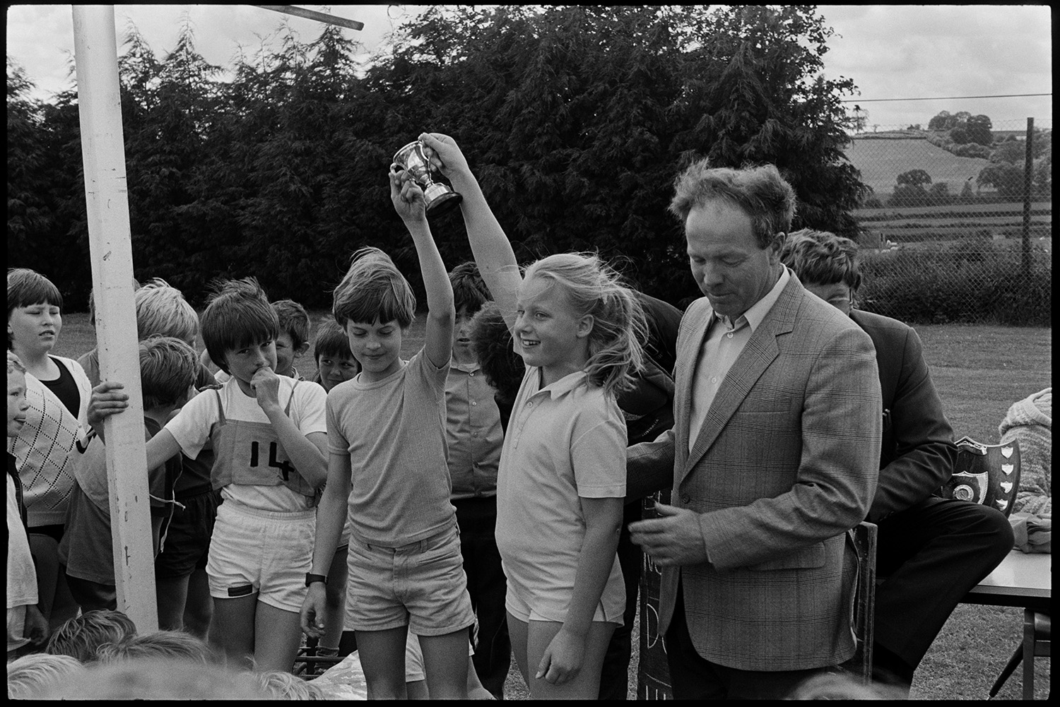 School sports day, children races, prize giving, cups. 
[A boy and girl holding up a trophy which they have won at a sports day where children from Black Torrington School, Northlew School, Dolton School and Highampton School were competing. The event was held on the school field at Winkleigh School.]