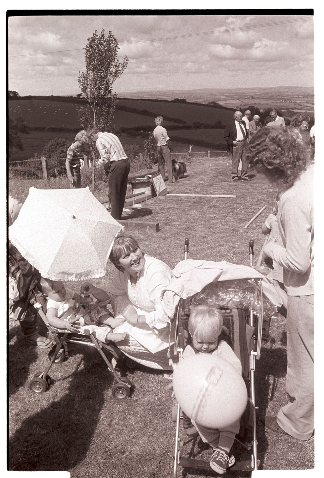 Mothers, women and children at fete, pushchairs, balloons. Babies. <br />
[Two mothers with their children in pushchairs at High Bickington Church Fete at the Rectory. A putting game is visible in the background.]