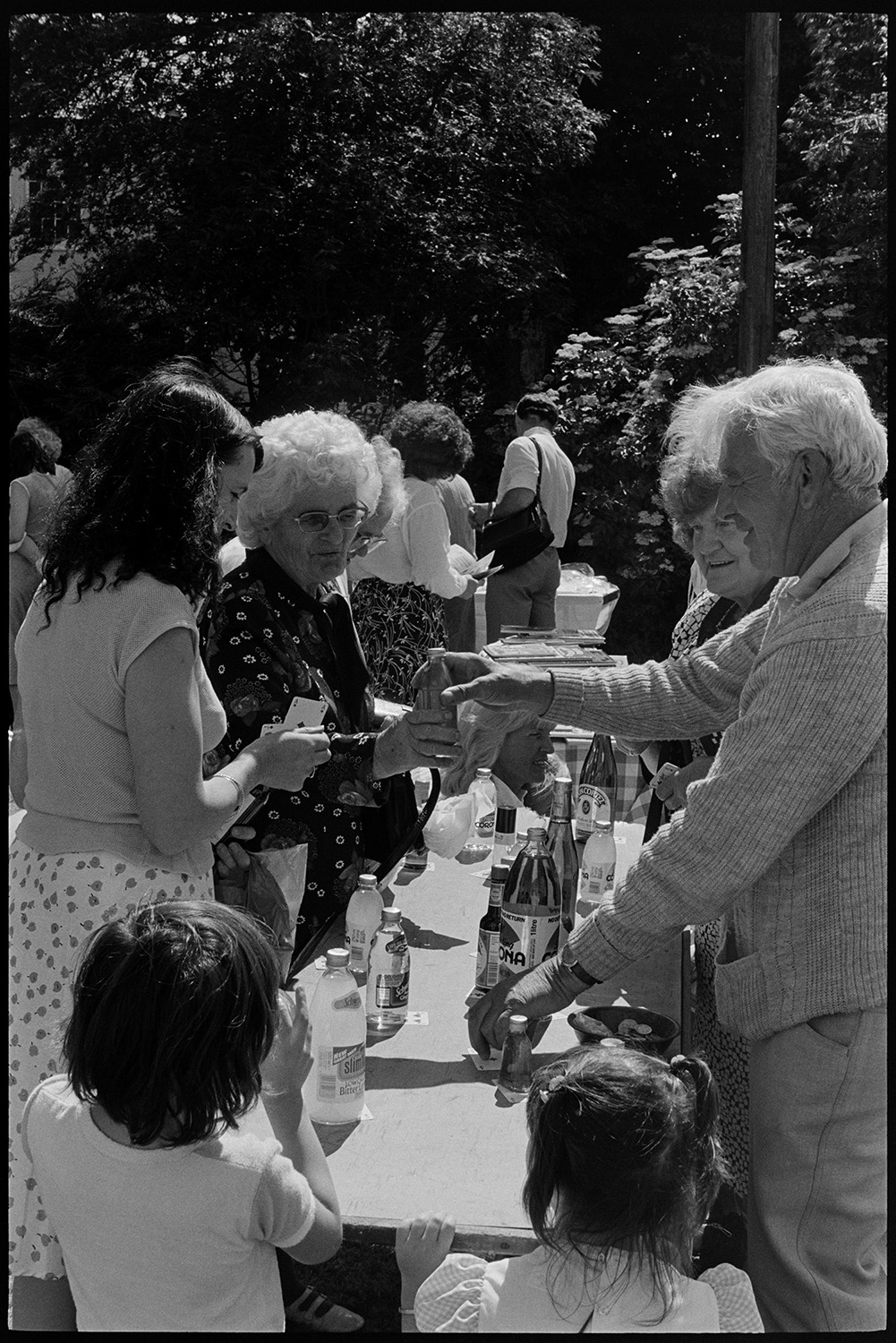 Stalls at fete, skittle alley cakes, raffle stall, pony ride. <br />
[Women and children having a go on a bottle stall at High Bickington church fete held at the vicarage.]