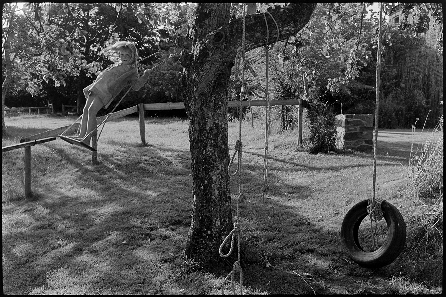 Little girl on swing in garden. 
[Sarah Wright playing on a swing attached to a tree in the garden at Barlands, Dolton. Various ropes and tyre swing are also attached to the tree.]