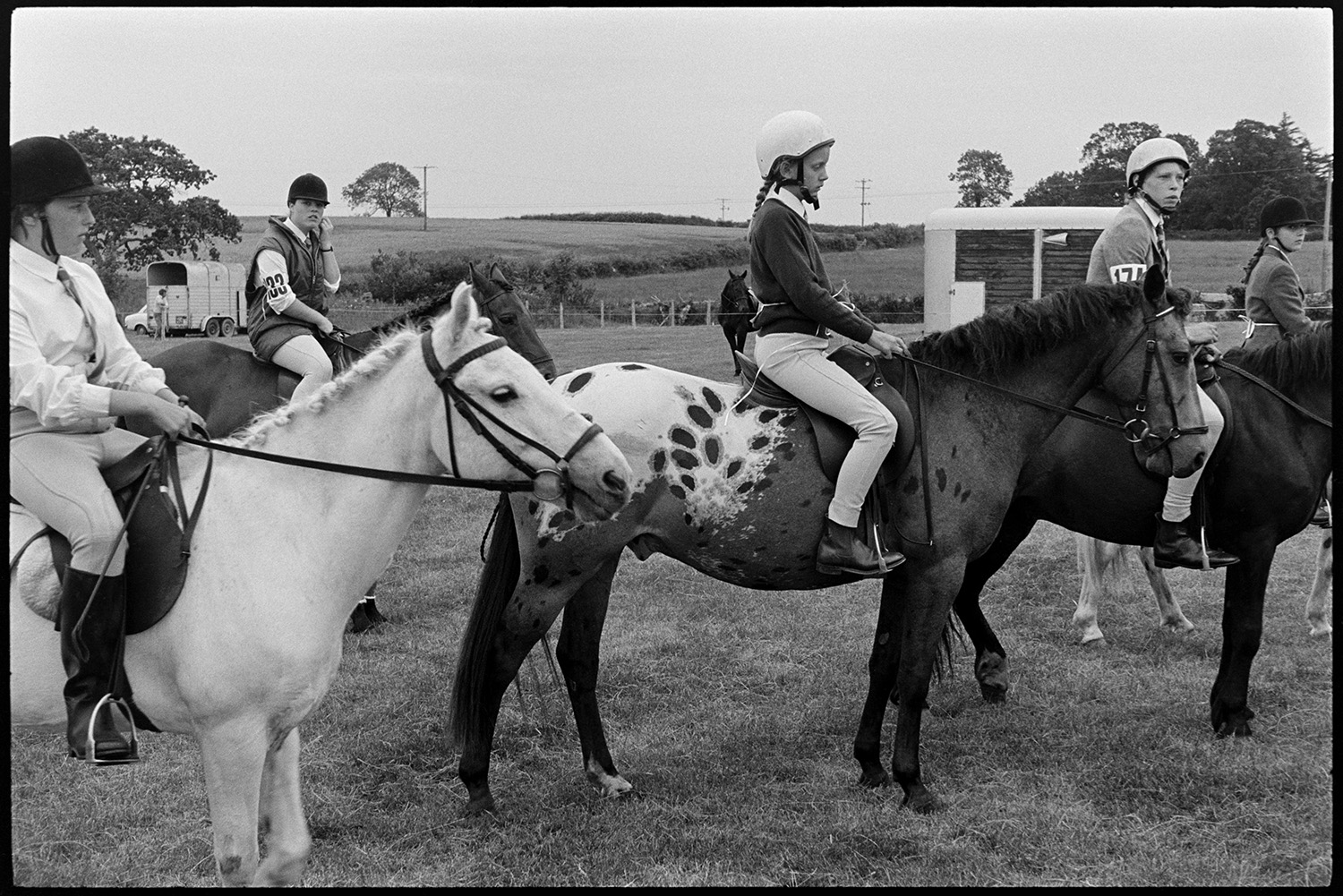 Gymkhana at Fair, horses, ponies and riders. Old bus. 
[Children on horses getting ready to compete in an event at the gymkhana at Winkleigh Fair. One of the horses has interesting markings.]