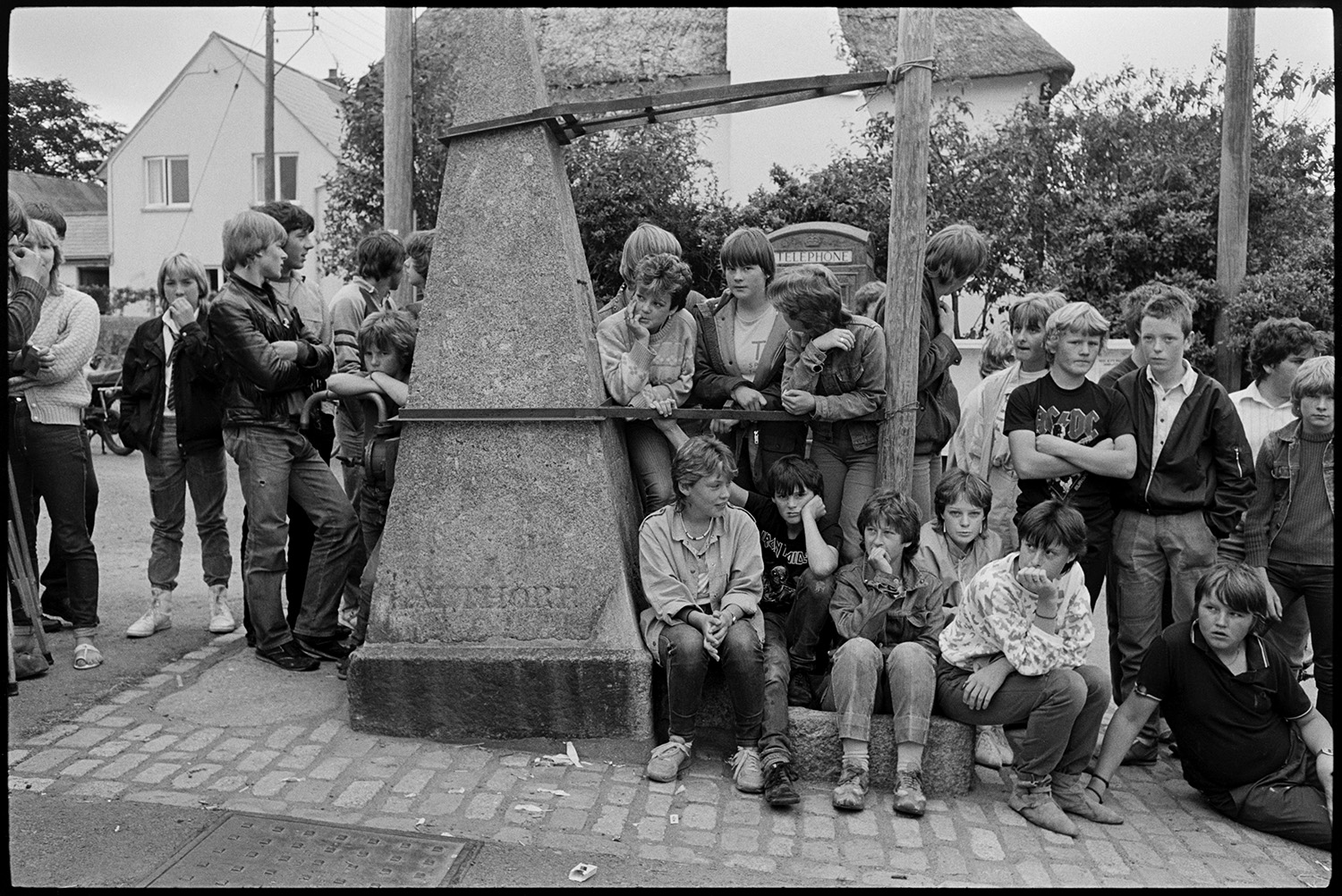 Fair Queen and attendants in village square, spectators waiting around. Photographer. 
[Children and teenagers gathered by the pump in Winkleigh village square for the start of Winkleigh Fair.]