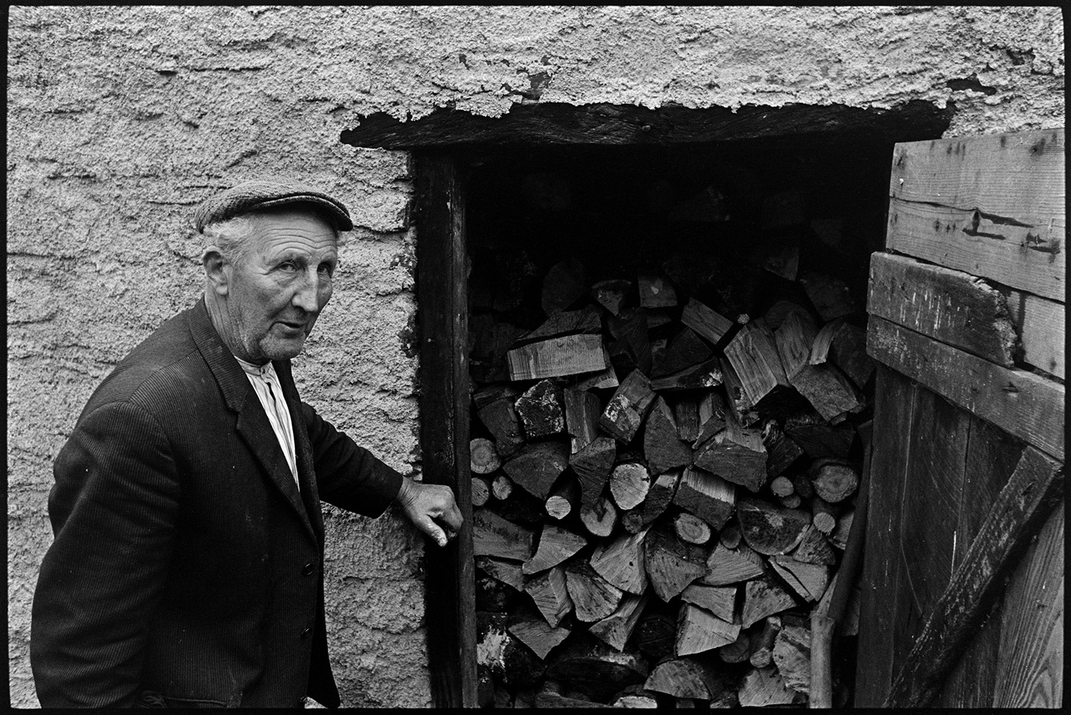 Doctor on rounds talking to man patient outside his house.
[Edward Cotsford stood by a shed with a  pile of logs at Charles Bottom, South Molton.]