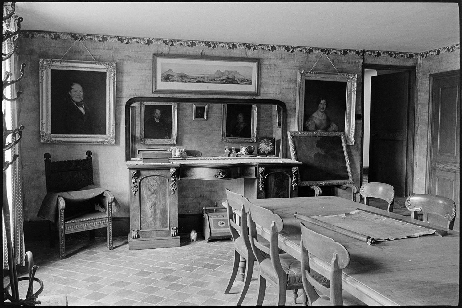 Dining room of large farmhouse. Furniture, table, chairs, mirror on sideboard. 
[The dining room at Narracott, South Molton with a large table, chairs, sideboard with mirror, a carved chair and pictures hung on the wall. An unrolled map is visible on the table.]
