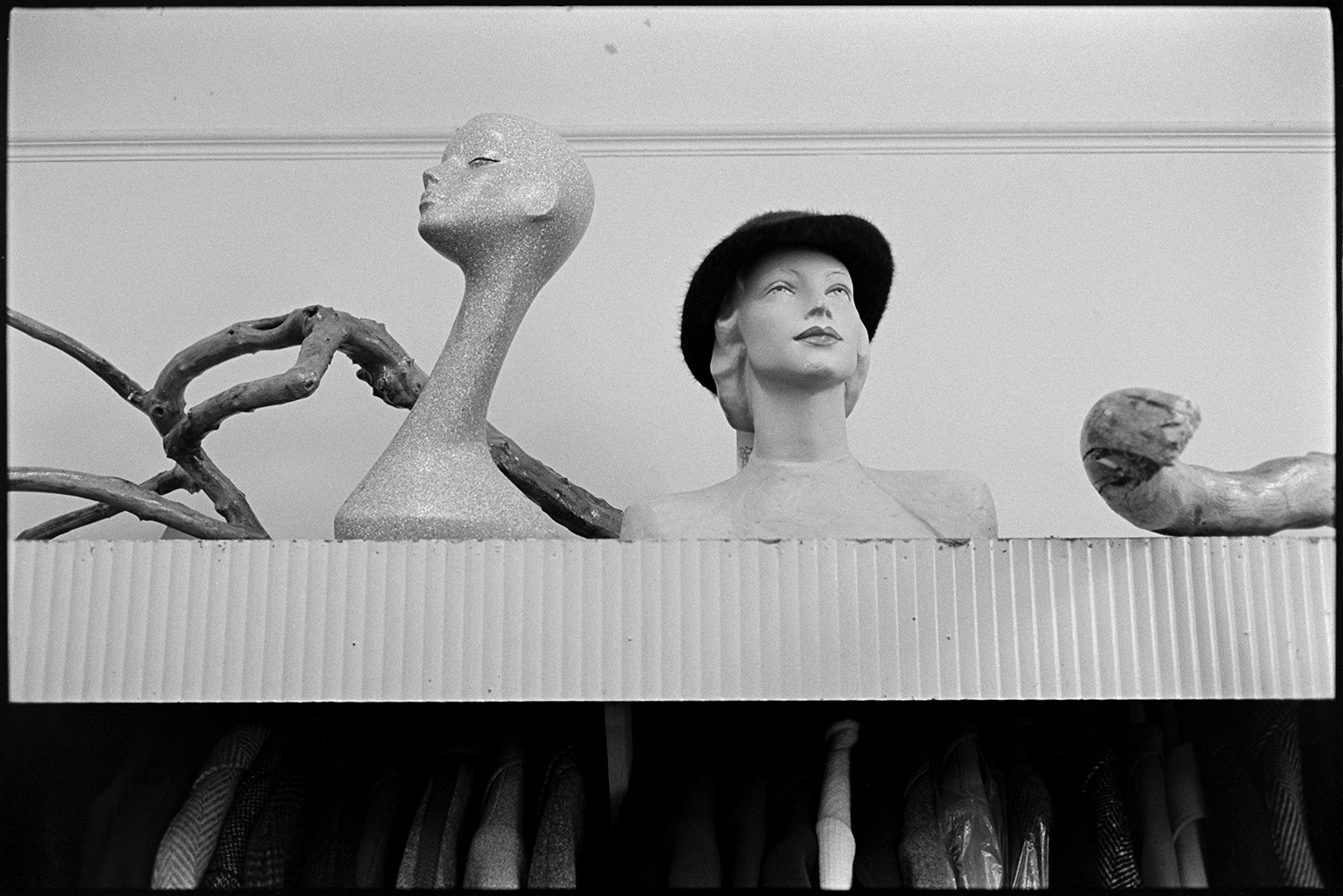 Shop assistant helping woman choose a hat in hat department of clothes shop. Hat display. 
[A hat display above a clothes rail in Trapnells clothes shop, in Bideford High Street. Driftwood is displayed by the mannequins with the hats.]