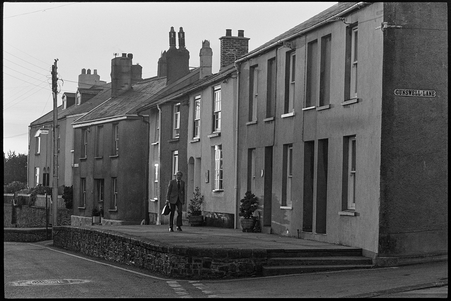 Doctor on rounds walking down street of terraced houses. 
[Doctor Richard Westcott walking past terraced houses in West Street, South Molton on his rounds to visit patients.]