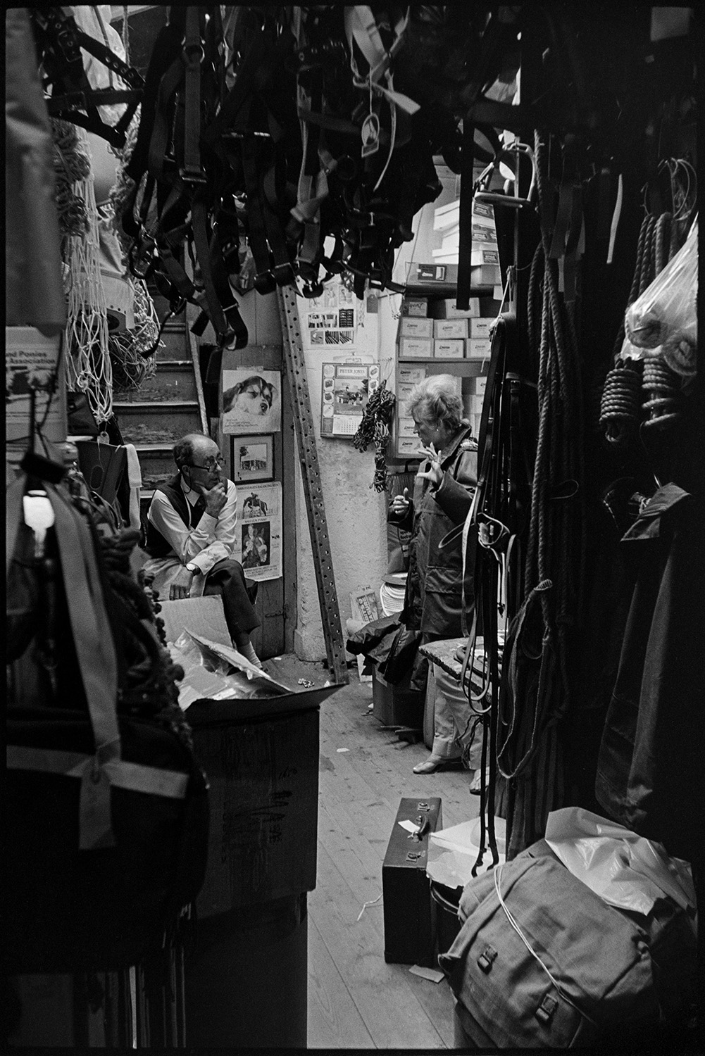 Saddlers shop, proprietor and customer. <br />
[Derek Johns serving a customer in his saddlers shop in Buttgarden Street, Bideford. Various goods are on display including ropes.]