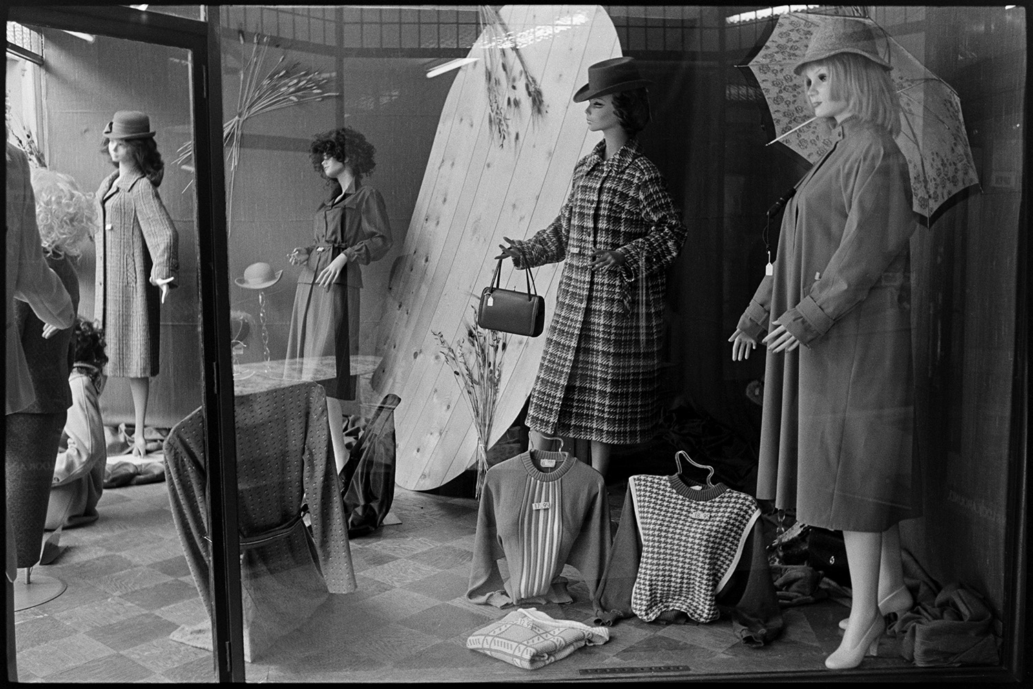 Window display of clothes shop. 
[The front window display in Trapnells clothes shop in Bideford High Street. Mannequins are modelling coats, hats, bags and umbrellas. Jumpers are also on display in the window.]