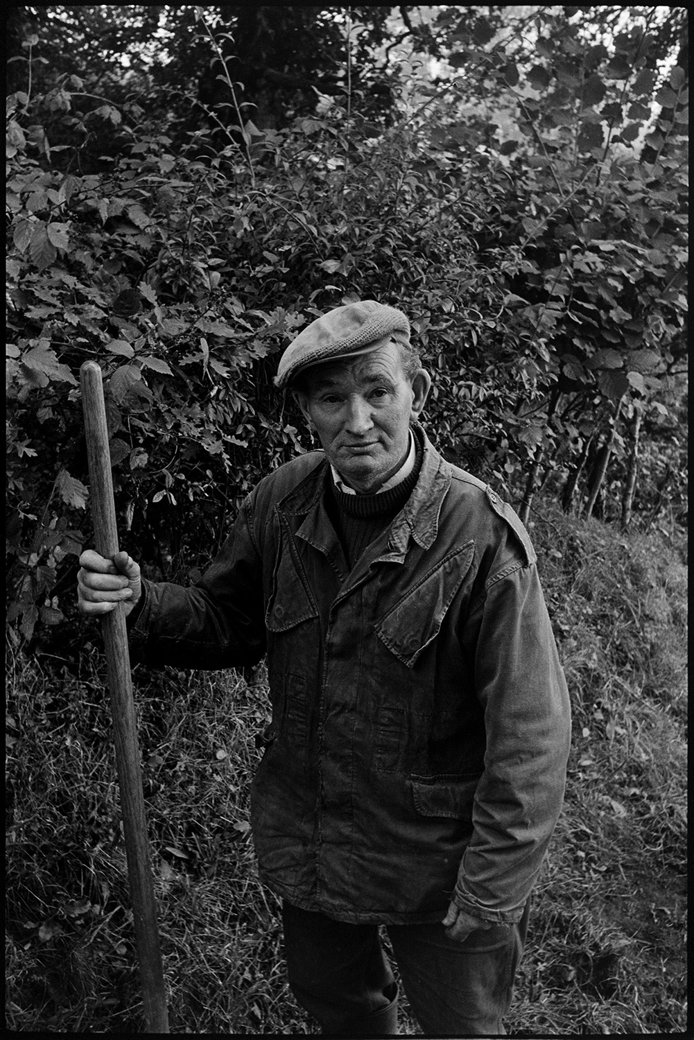 Man cleaning out ditch on road to farm. Spade. 
[Bill Lott stood holding a spade by a hedgerow after clearing a ditch by a roadside at Westpark, Iddesleigh.]