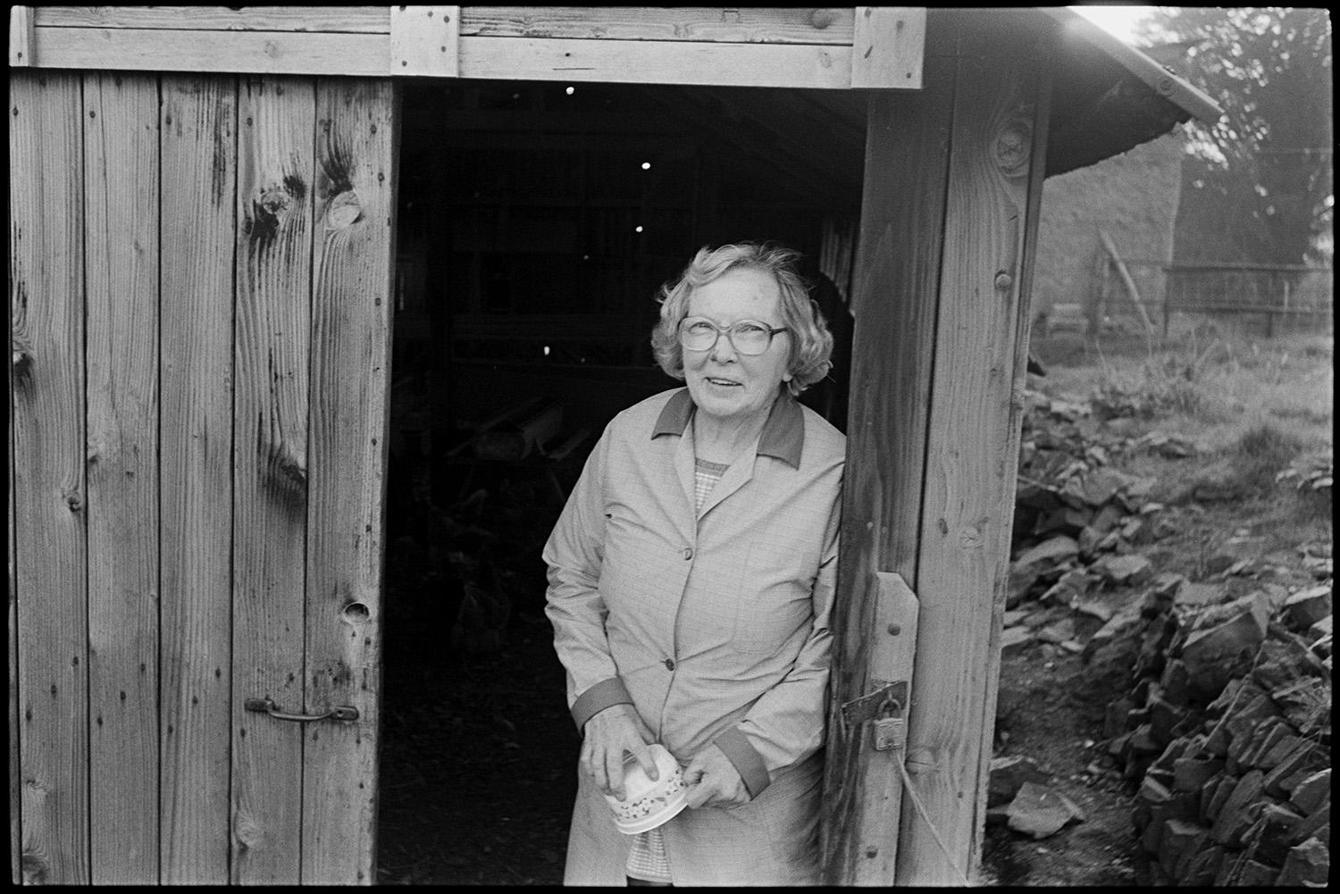 Farmers wife woman feeding chickens. 
[May Pugsley stood at the entrance to a wooden poultry house at Lower Langham, Dolton. She has been feeding the chickens in the poultry house.]