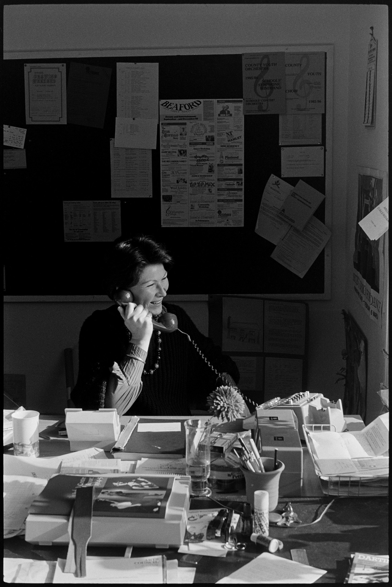 Arts administrator in office on telephone. 
[Shirley Thomas using a telephone in the office at the Beaford Centre at Greenwarren House in Beaford. Various papers are on the desk in front of her.]