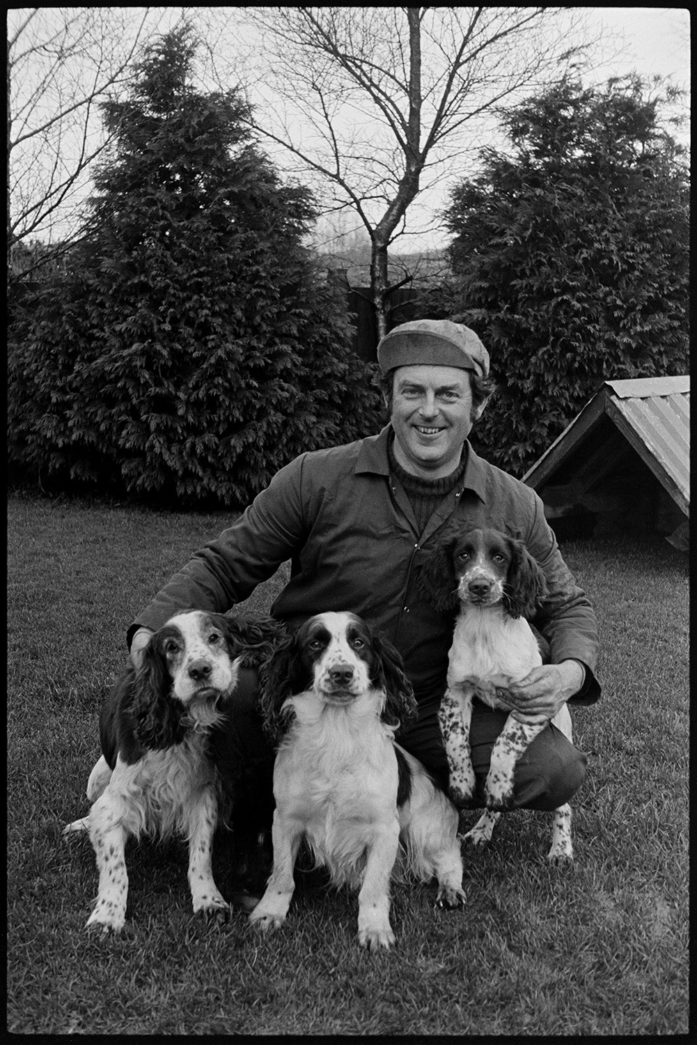 Man and his dogs. 
[Chris Styles with three spaniel dogs on a lawn at Langham, Dolton.]